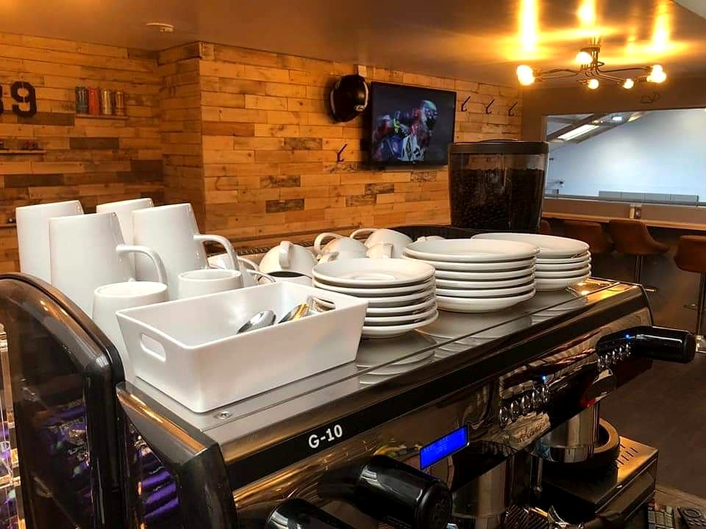 The café counter: white cups and plates stacked on the coffee machine, timber-clad wall behind