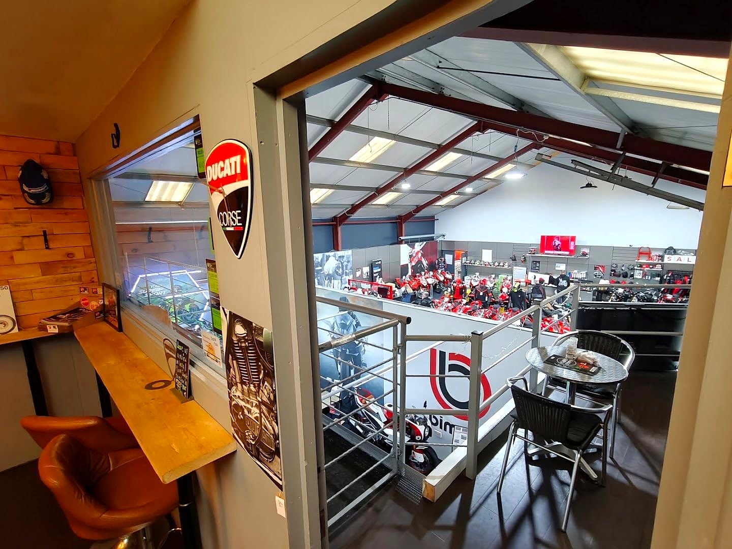 Looking down from the café's raised seating area into the Ducati showroom, red bikes on the floor below